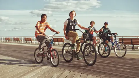 Group lifestyle photograph of cyclists riding together along a seaside boardwalk; coordinated movement and open space communicate community, health and shared momentum.