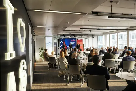 Wide establishing photograph of a business conference in a modern venue, showing the audience, stage, presentation screen and spatial relationship of the event.