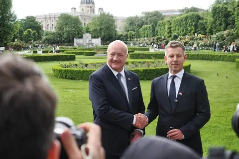Documentary handshake between two suited men in a formal garden setting, observed by press and guests; the frame captures protocol, relationship and public significance.