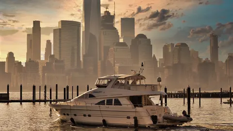 White yacht moored against the Manhattan skyline at sunset; warm haze, water and architecture combine luxury, distance and metropolitan aspiration.