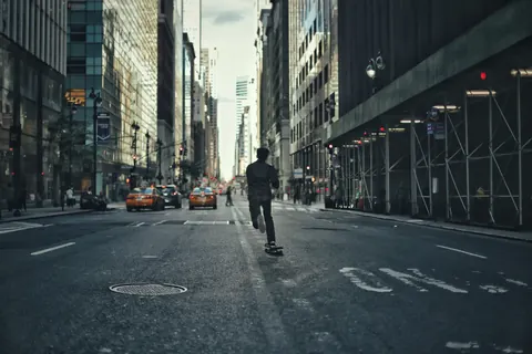 Lone person moving down the centre of a New York street between traffic and scaffolding; the deep urban corridor frames a narrative of autonomy and motion.