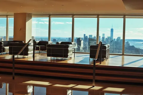 Minimal modern lounge with chairs facing floor-to-ceiling windows and the Manhattan skyline; architecture and view communicate calm, privilege and strategic perspective.