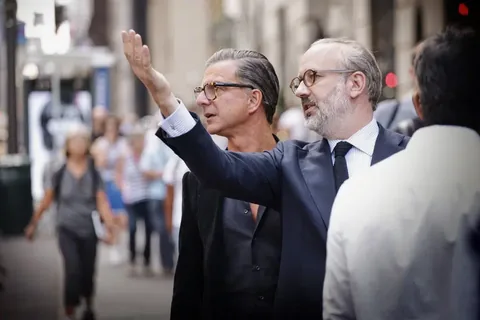 Candid leadership photograph of two suited men in conversation on a city street, one gesturing toward the surroundings; the image combines executive presence with…