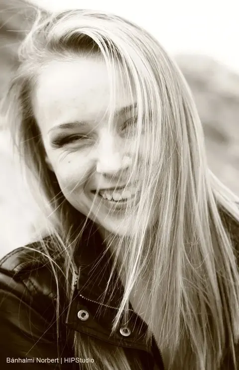 Monochrome outdoor portrait of a laughing young woman with windblown hair; spontaneous expression and close crop create a vivid sense of freedom.
