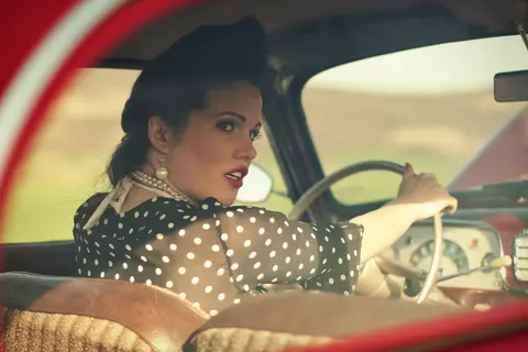 Second frame of the vintage car portrait, showing the woman’s poised profile, gloved hand and classic interior; the cinematic treatment reinforces a controlled…